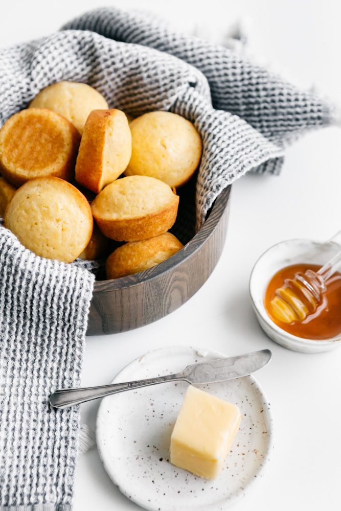 A bowl of cornbread muffins with butter and honey 