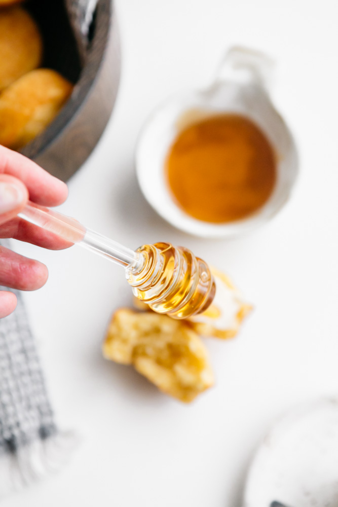 A glass honey stick with honey dripping down. 