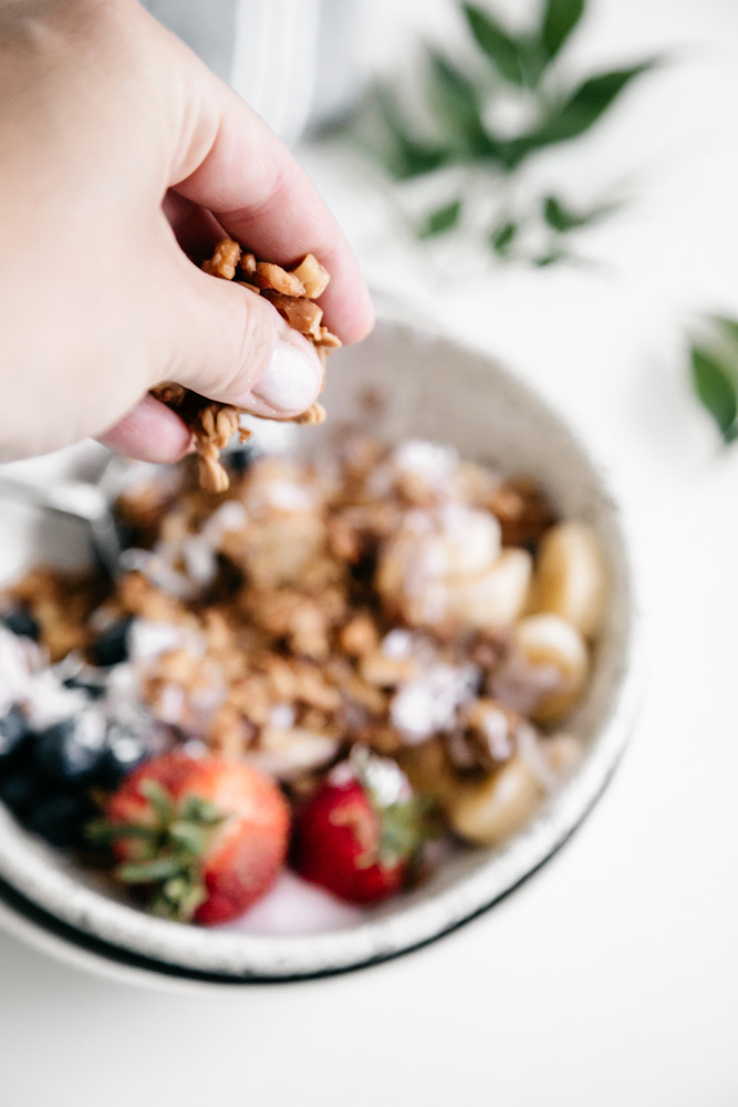 Sprinkling granola onto breakfast bowl. 