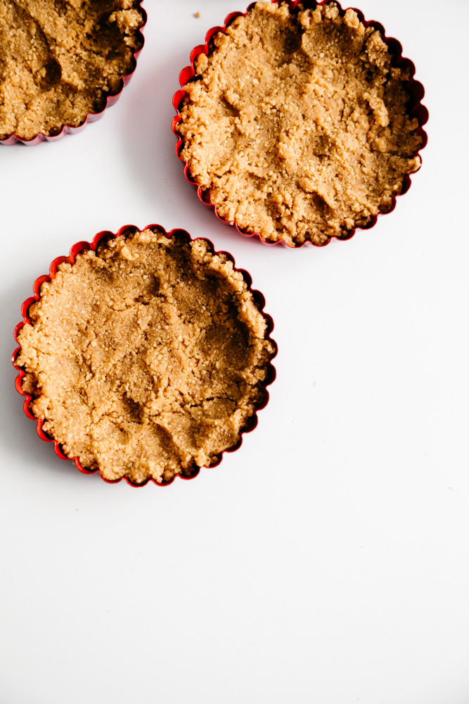 Graham cracker crust in tart pans for creamy grapefruit curd mini tarts. 