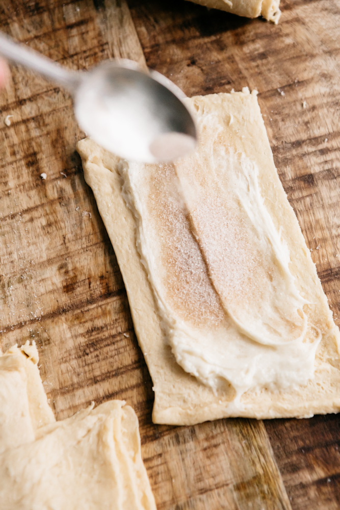 Sprinkling cinnamon and sugar onto unrolled pastry dough 