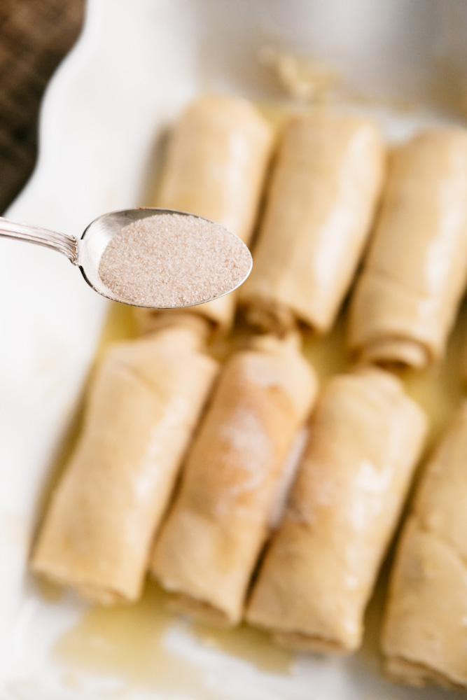 Sprinkling cinnamon and sugar onto pan of crescent pastries. 