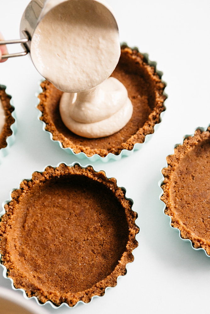 Pouring cheesecake filling into tart crusts 