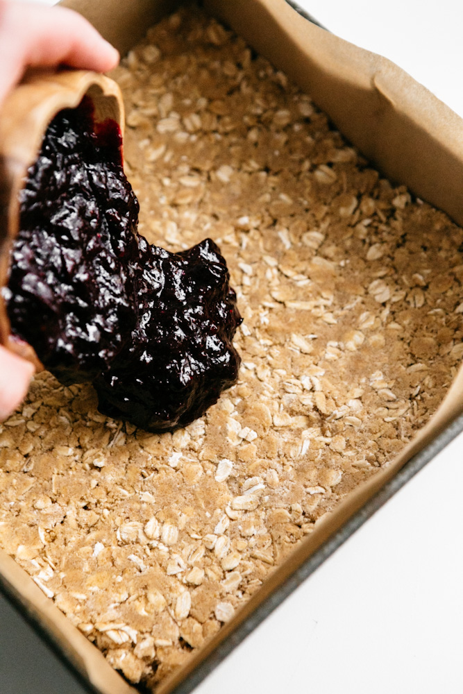 Pouring blueberry preserves over crumbly crust 