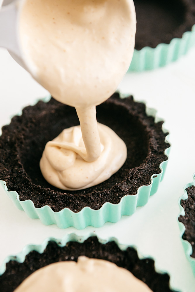 Pouring peanut butter cheesecake filling into oreo crust tart pans 