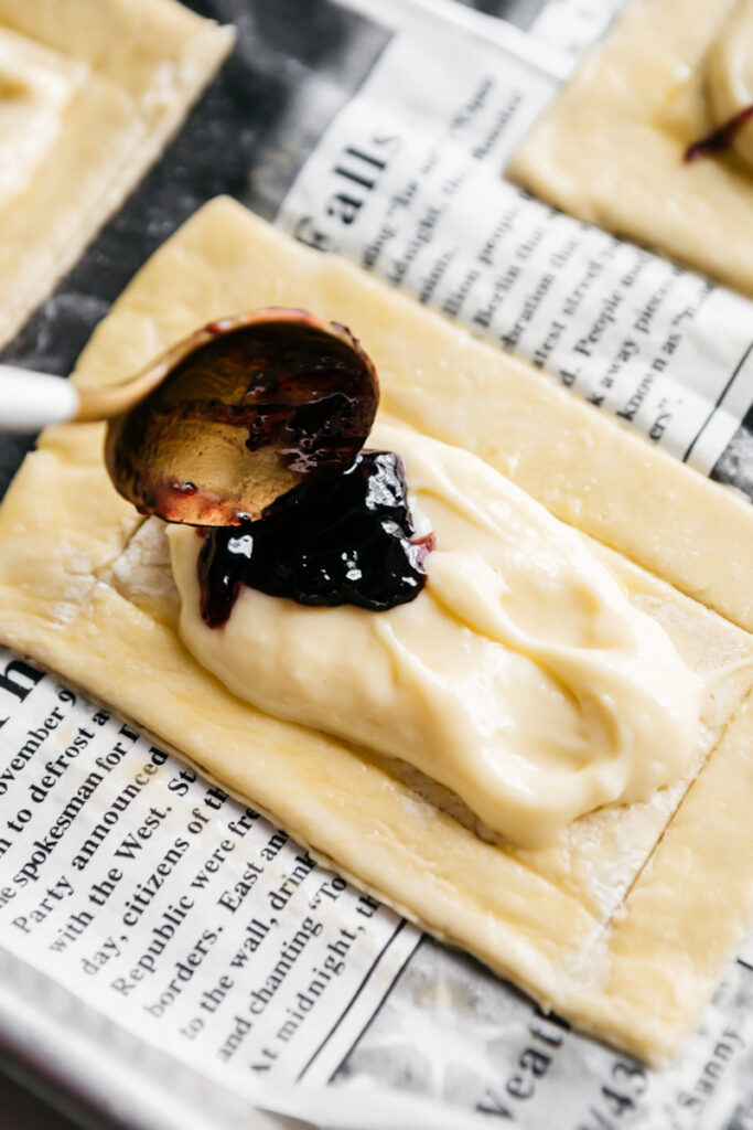 Spooning preserves onto cheesecake topped puff pastries 