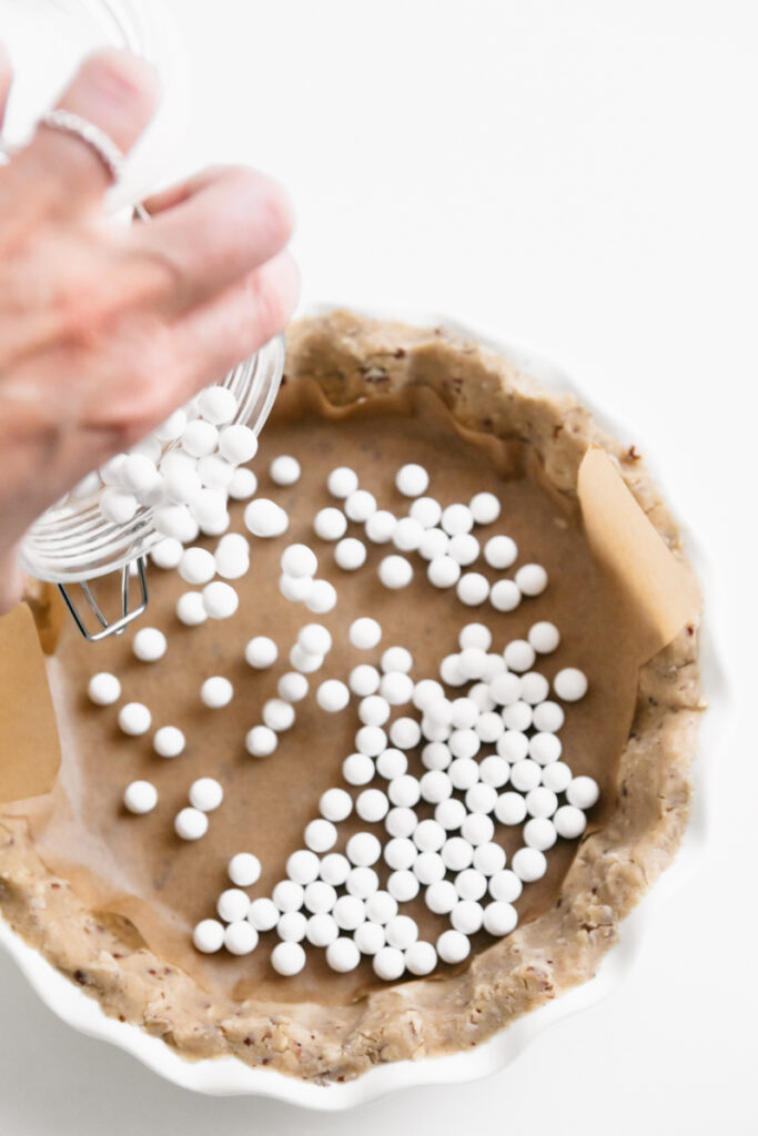 Pouring white pie weights into pie crust 