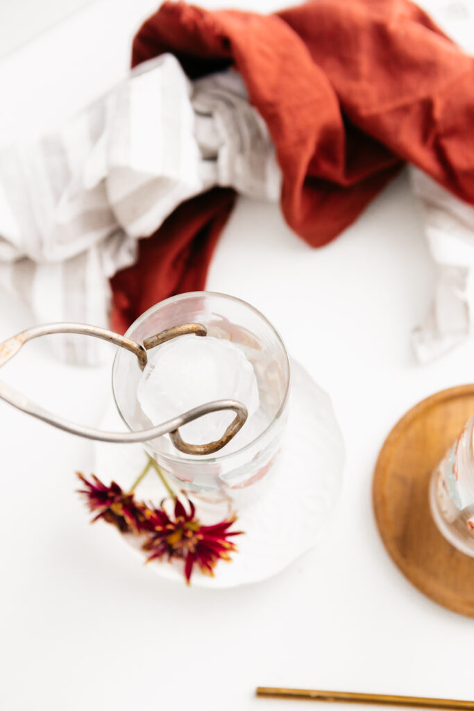 Placing a large ice cube in a glass with tongs 