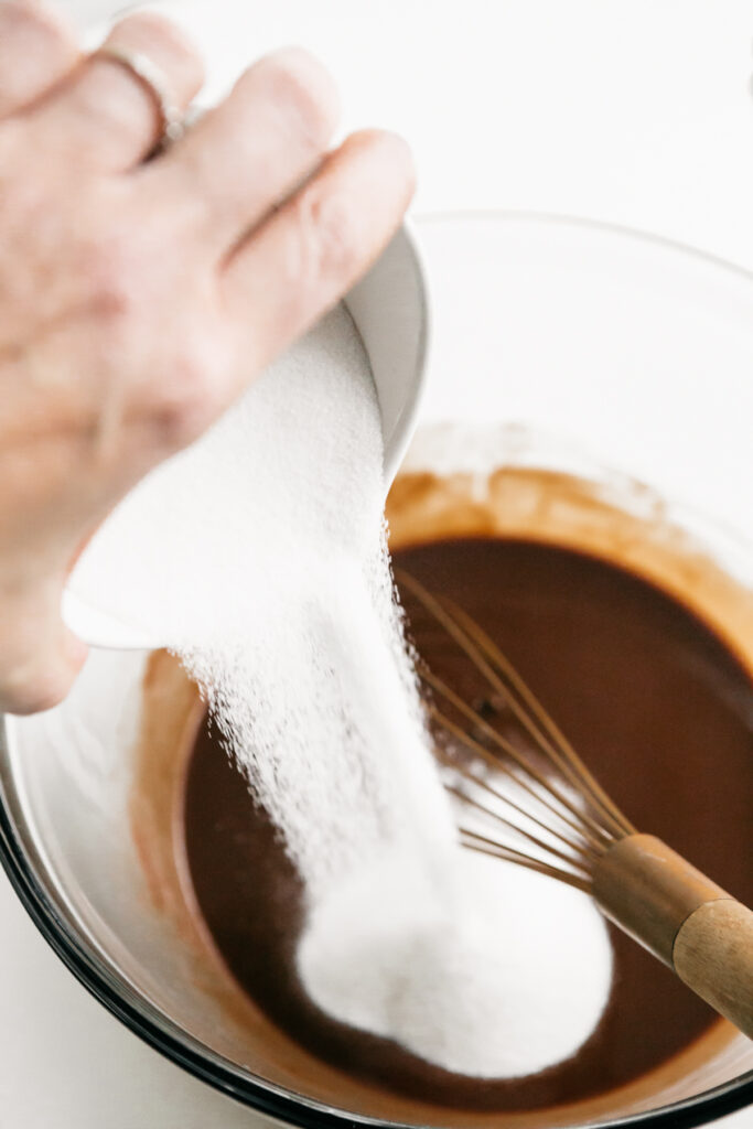 Pouring sugar into a bowl of brownie batter