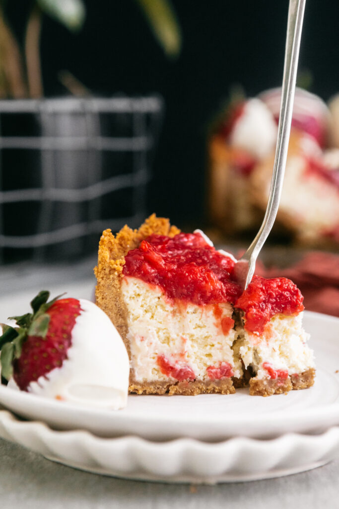 A slice of strawberry cheesecake with a fork in it 